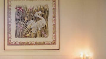 Un cuarto de spa con una obra enmarcada de pájaros y juncos en la pared, una bañera con velas sobre una mesita auxiliar y una fuente de agua visible.