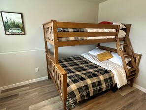 Ein Stockbett mit karierter Bettdecke und Kissen, ein Holz-Kopfteil und ein an der Wand hängendes Bild von einem Lieferwagen.