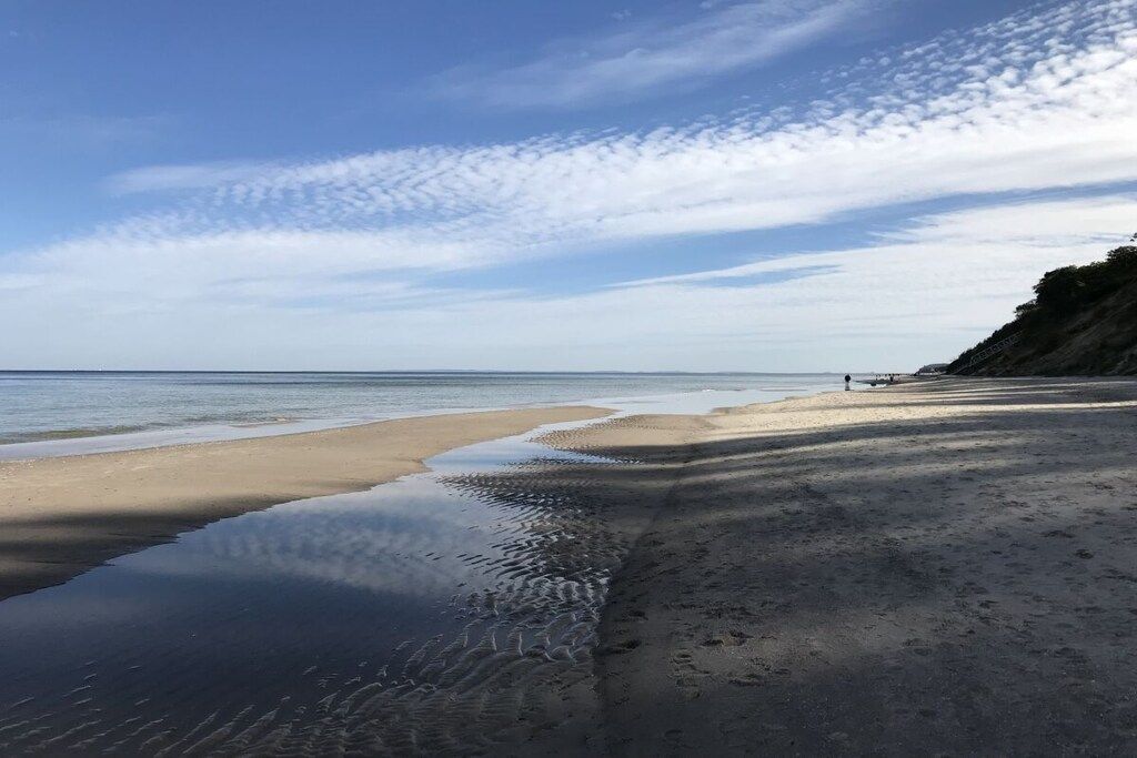A beach with a calm sea, a sandy shore, and a clear sky.