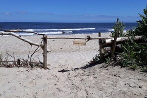 Ein Strand mit Holzlattenzaun und einem Schild, feinem Sand und Meereswellen.