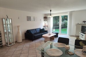 Een woonkamer met een glazen salontafel, een zwarte bank en een eettafel met plaatsmatten.