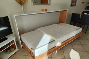 A room with a bed, a TV on a stand, a small table with two orange cups, and a chair. - Holiday apartment "Horumersiel" (Wangerland)