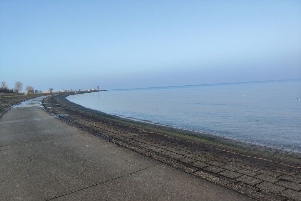 Un sendero pavimentado a lo largo de una masa de agua tranquila, con un cielo despejado.