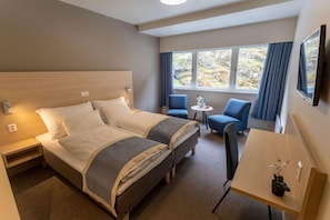 A hotel room with a bed, a desk, two chairs, a small table, and a window with curtains. - Laerdal (Laerdal)