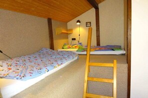 Ein Zimmer mit zwei Etagenbetten, einer Holzleiter, einem Schreibtisch mit Lampe und einem an der Wand befestigten Regal.