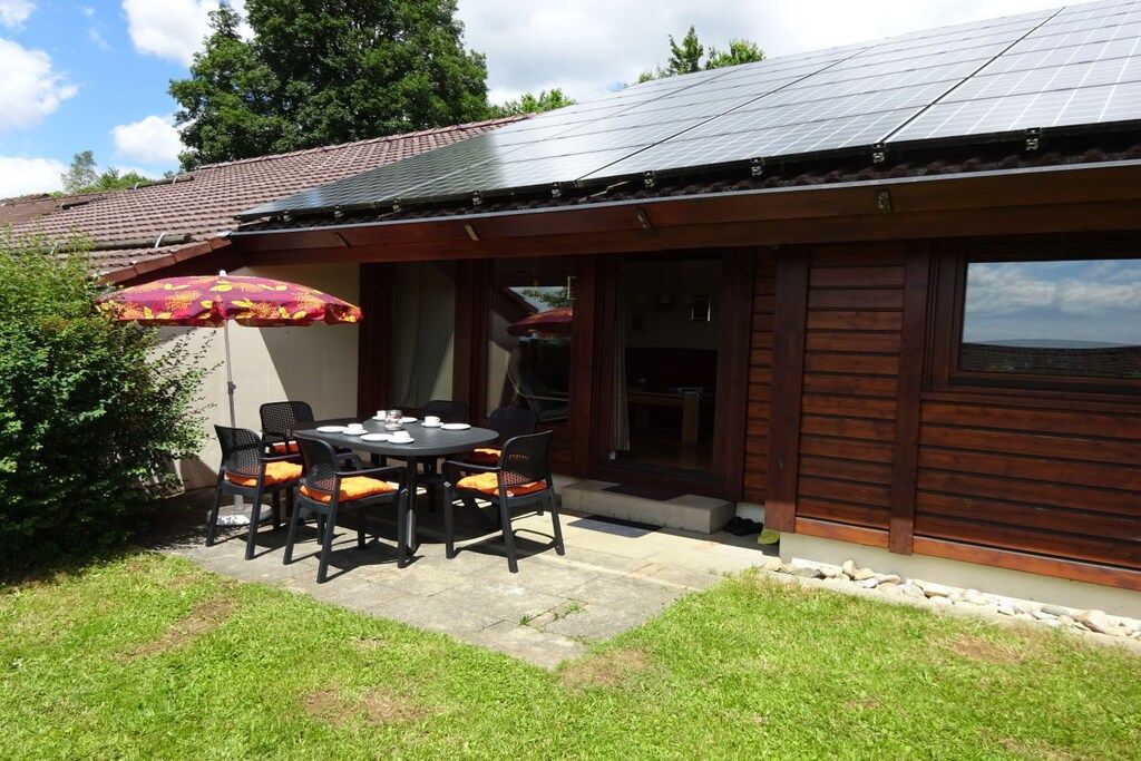 Edificio de madera con techo de paneles solares, un patio con mesa y sillas, y un paraguas grande.