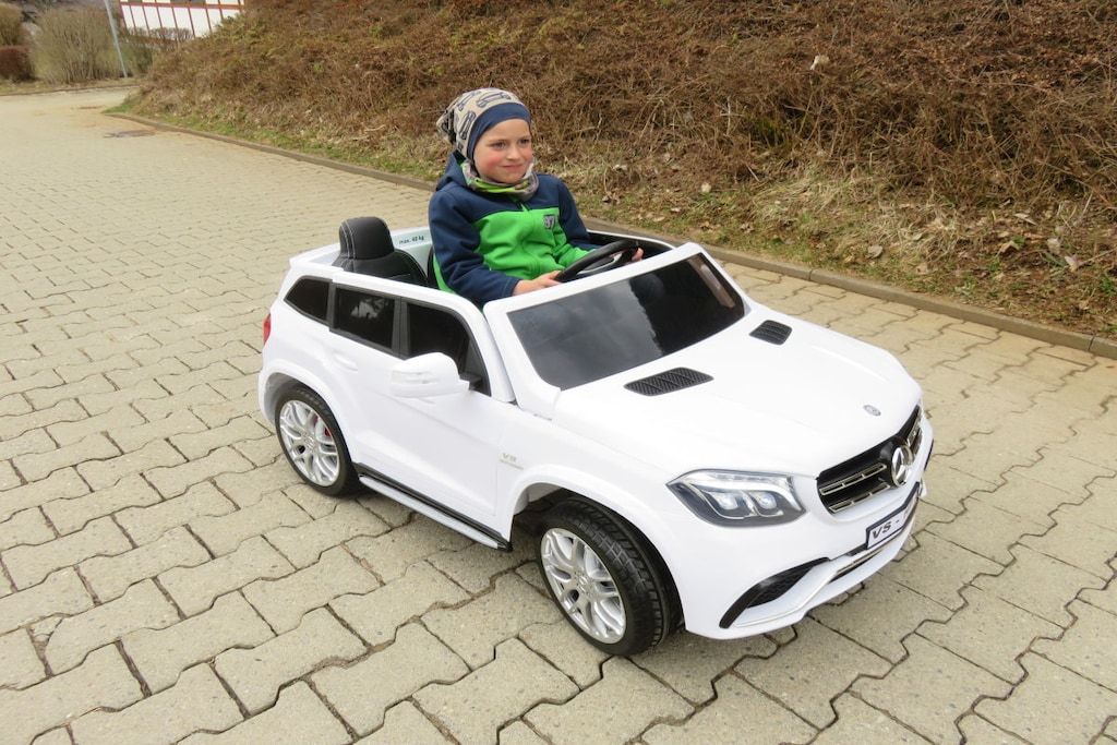 A child in a white toy car on a paved surface.