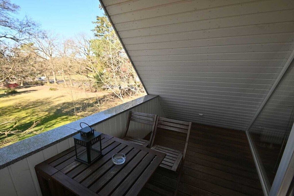 A balcony with a wooden table and chairs, a lantern, and a view of a yard with trees and a car.