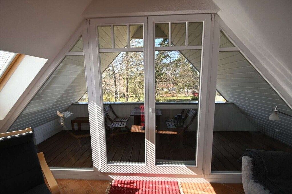 A room with a sloped ceiling, a sliding glass door leading to an outdoor deck, and a small table with chairs.