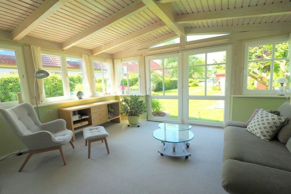 Ein Zimmer mit Holzboden, einem Glastisch, einer Couch, einem Sessel und einem Schreibtisch mit Pflanze.