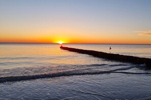 A sunset over a calm sea with a wooden pier extending into the water. - Peter's holiday home (Ostseebad Ahrenshoop)