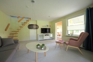 A modern living room with a sofa, a coffee table, a pink chair, a TV, and a staircase. - Peter's holiday home (Ostseebad Ahrenshoop)