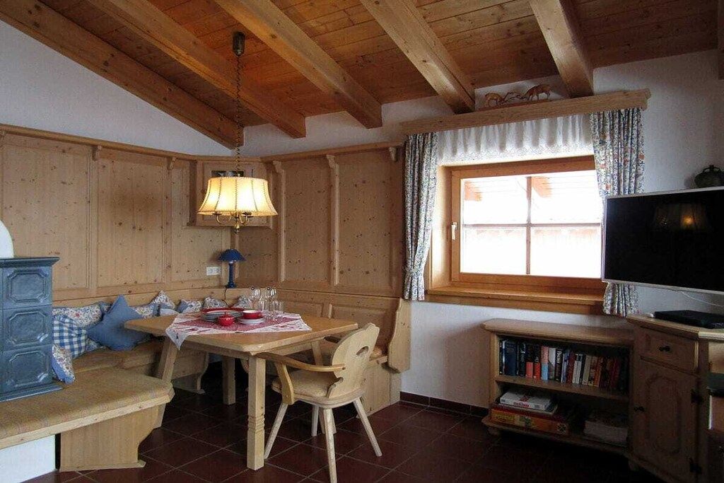 A cozy room with a wooden ceiling, a dining table with chairs, a bench, a television, and a bookshelf.