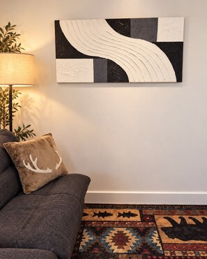 A living room with a sofa, a patterned rug, and a wall-mounted abstract artwork.