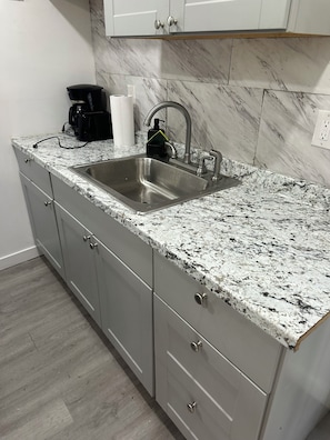 A kitchen with a granite countertop, stainless steel sink, and grey cabinets.