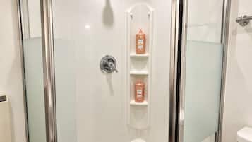 A modern shower enclosure with a glass door, a handheld showerhead, and a shelf with toiletries.