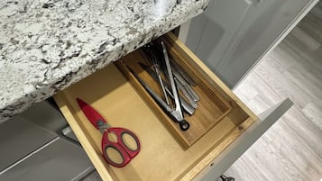 Un tiroir de cuisine contenant des ustensiles, une paire de ciseaux et une planche à découper.