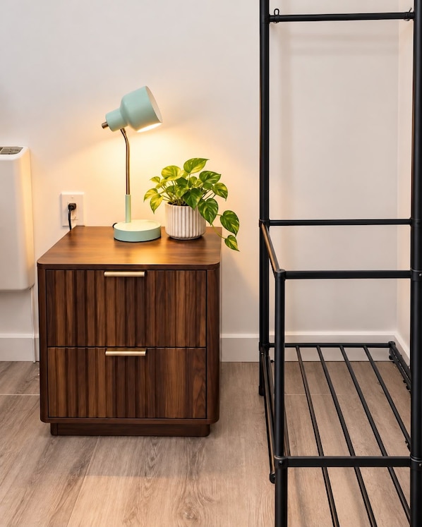 A wooden bedside table with a lamp and a potted plant.