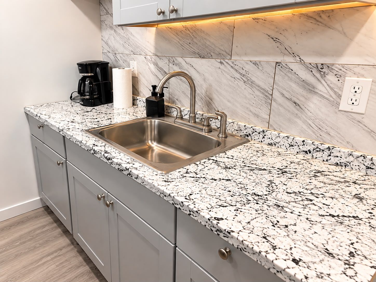 A kitchen with a stainless steel sink, granite countertop, and a marble backsplash.