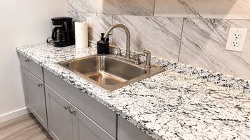 A kitchen with a stainless steel sink, granite countertop, and a marble backsplash.