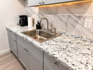 A kitchen with a stainless steel sink, granite countertop, and a marble backsplash.