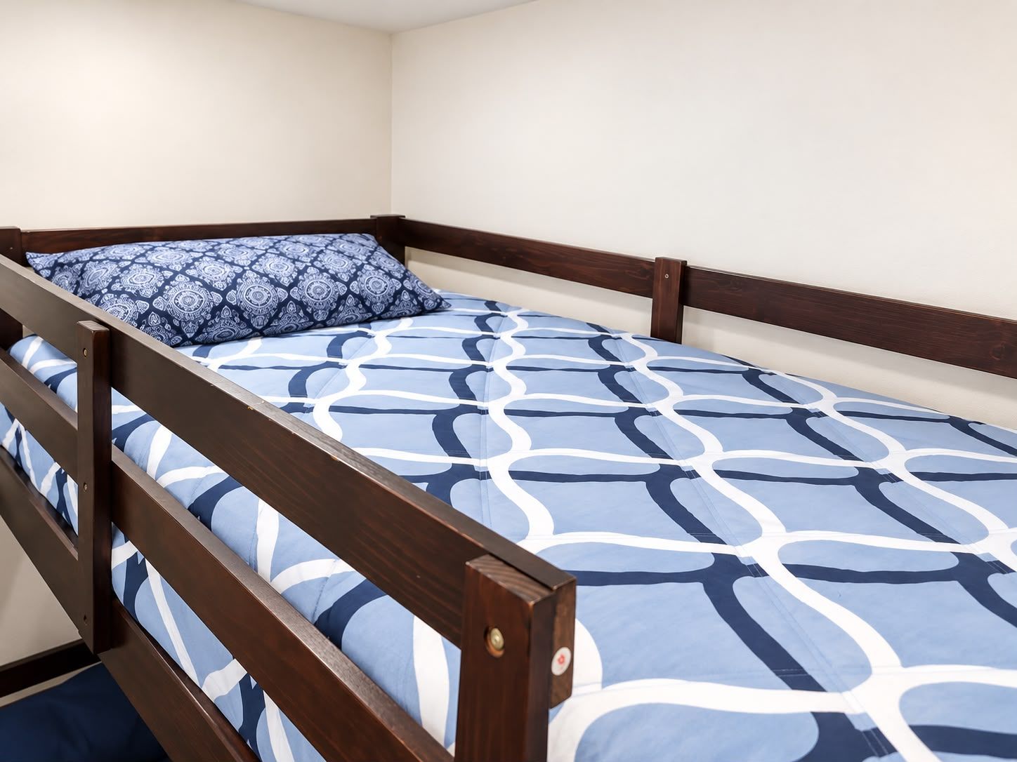Un lit simple avec un cadre en bois et une couvre-lit à motifs bleus.