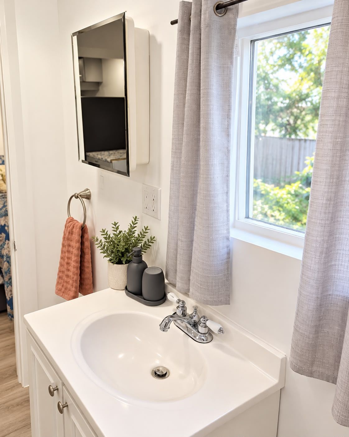 A bathroom with a white sink, a mirror, a towel rack, and a window with curtains.