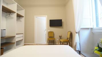 A bedroom with a bed, a wardrobe, two chairs, a television, and a window with curtains.
