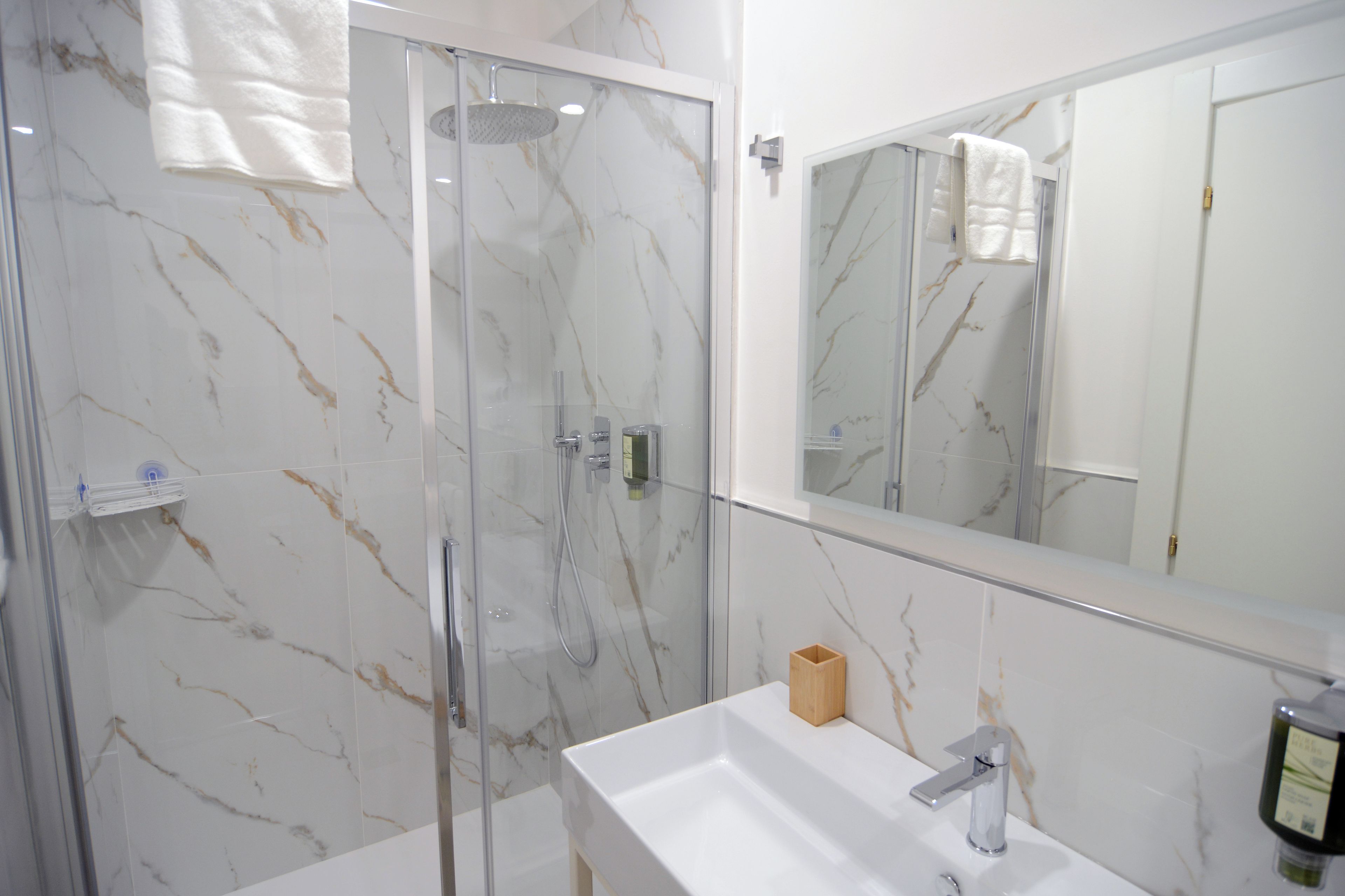 A modern bathroom with a glass-enclosed shower, a white sink, and a large mirror.