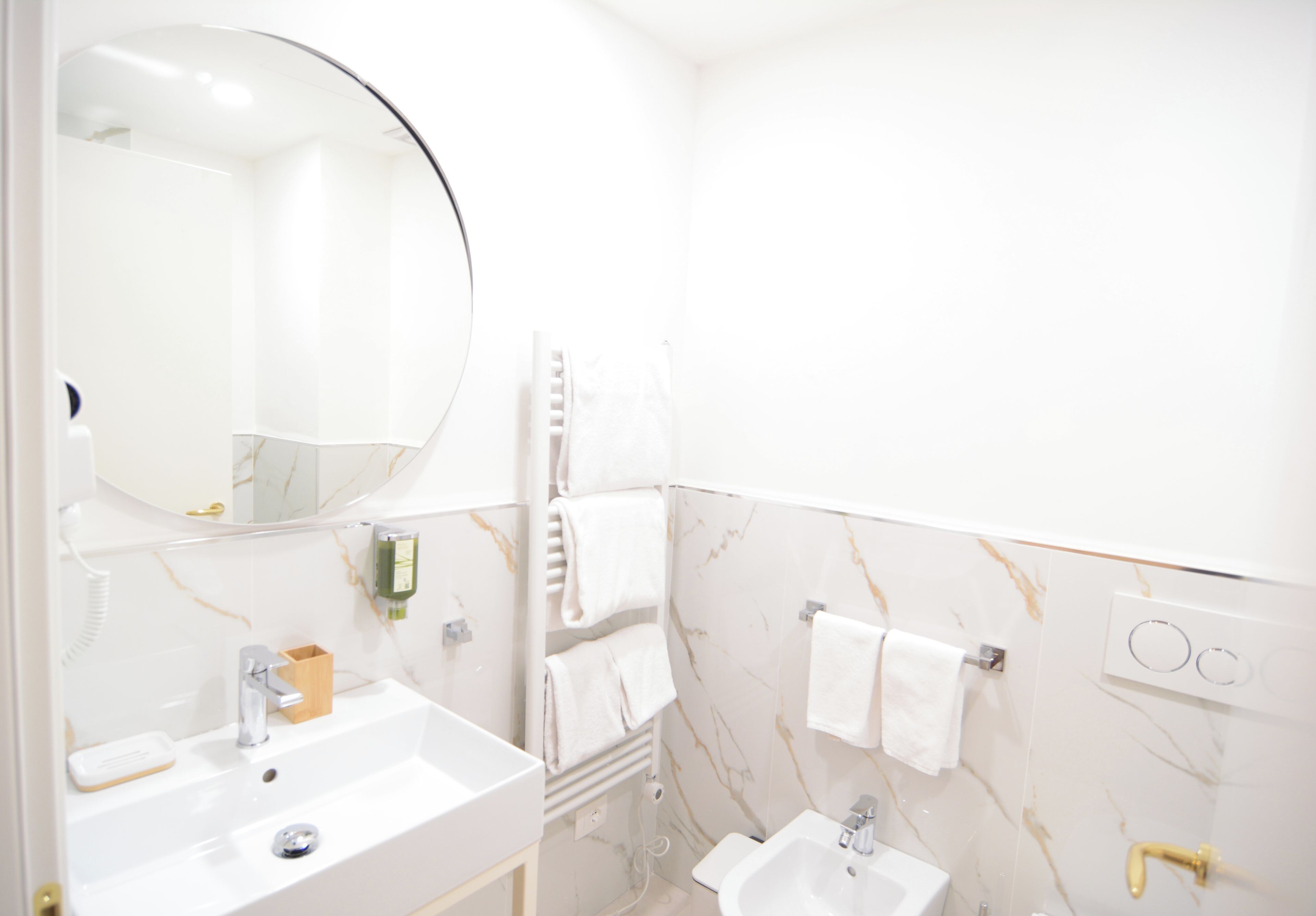 Une salle de bain avec un grand miroir rond, deux vasques, un porte-serviettes et un mur décoré d’un motif imitant le marbre.