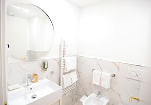 A bathroom with a round mirror, two sinks, a towel rack, and a marble-patterned wall. - Residenze Strozzi Firenze (Florence)
