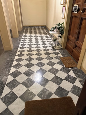 Un pasillo con piso a cuadros, una puerta de madera y una mesita con una planta.
