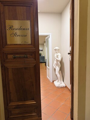 A wooden door with a plaque reading 'Residence Strozki 1st Piano' and a white statue of a figure on the floor.