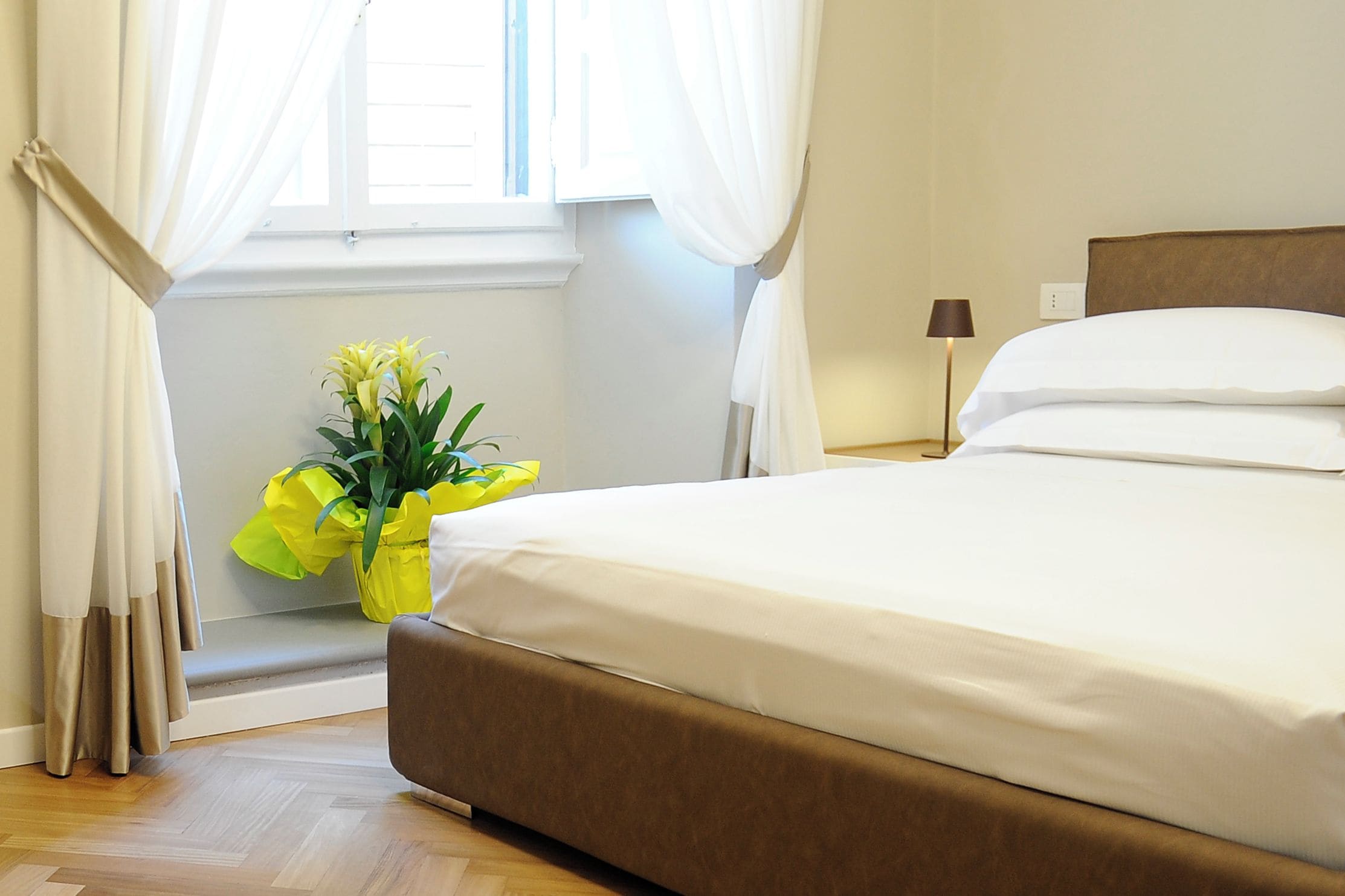 Une chambre d’hôtel avec un lit, des rideaux, une lampe de chevet et une fenêtre également dotée de rideaux.