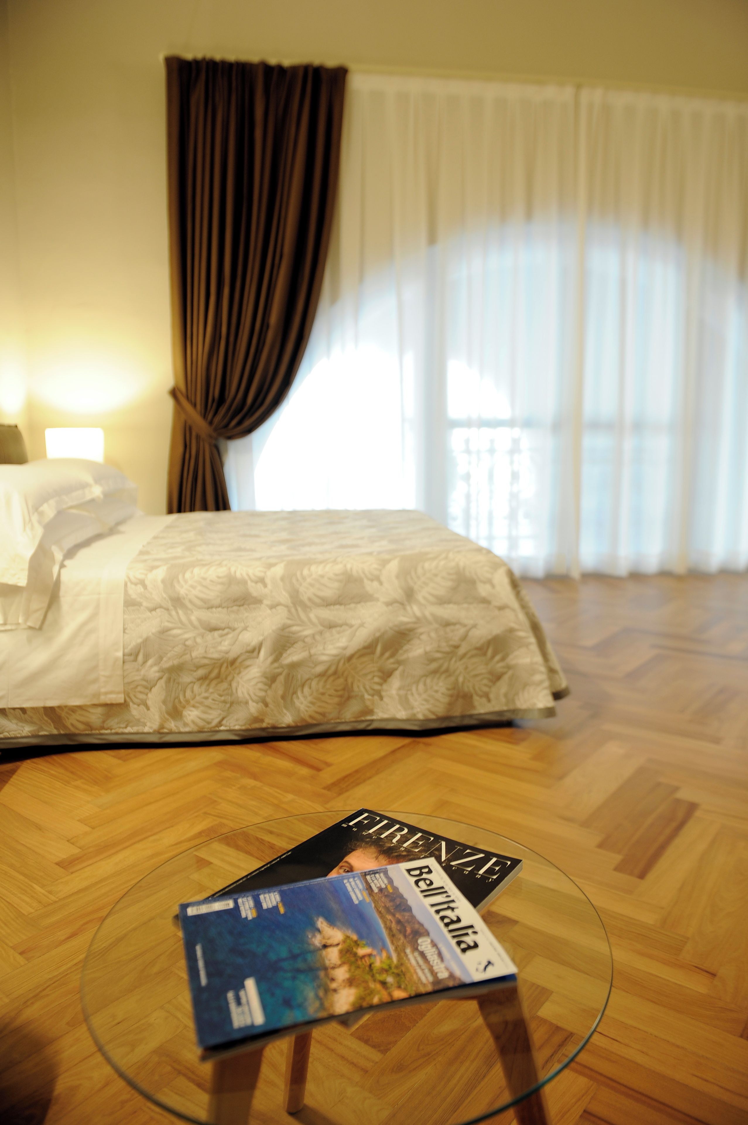 Ein Hotelzimmer mit einem Bett, einem Glastisch mit einer Zeitschrift und einem Fenster mit Vorhängen.