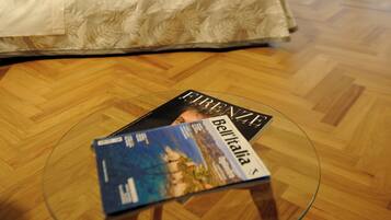 Ein Hotelzimmer mit einem Bett, einem Glastisch mit einer Zeitschrift und einem Fenster mit Vorhängen.