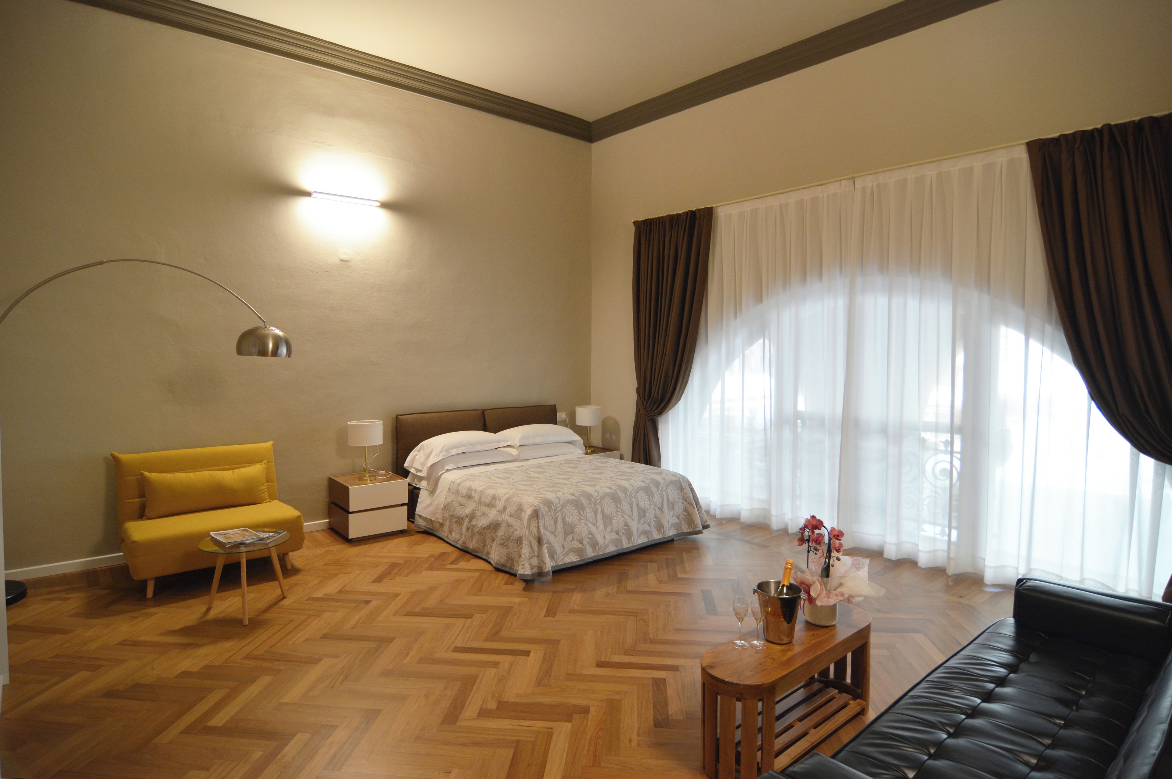 Ein Hotelzimmer mit einem Bett, einem gelben Sessel, einem schwarzen Sofa, einem Holztisch und einem Nachttisch mit Lampen.