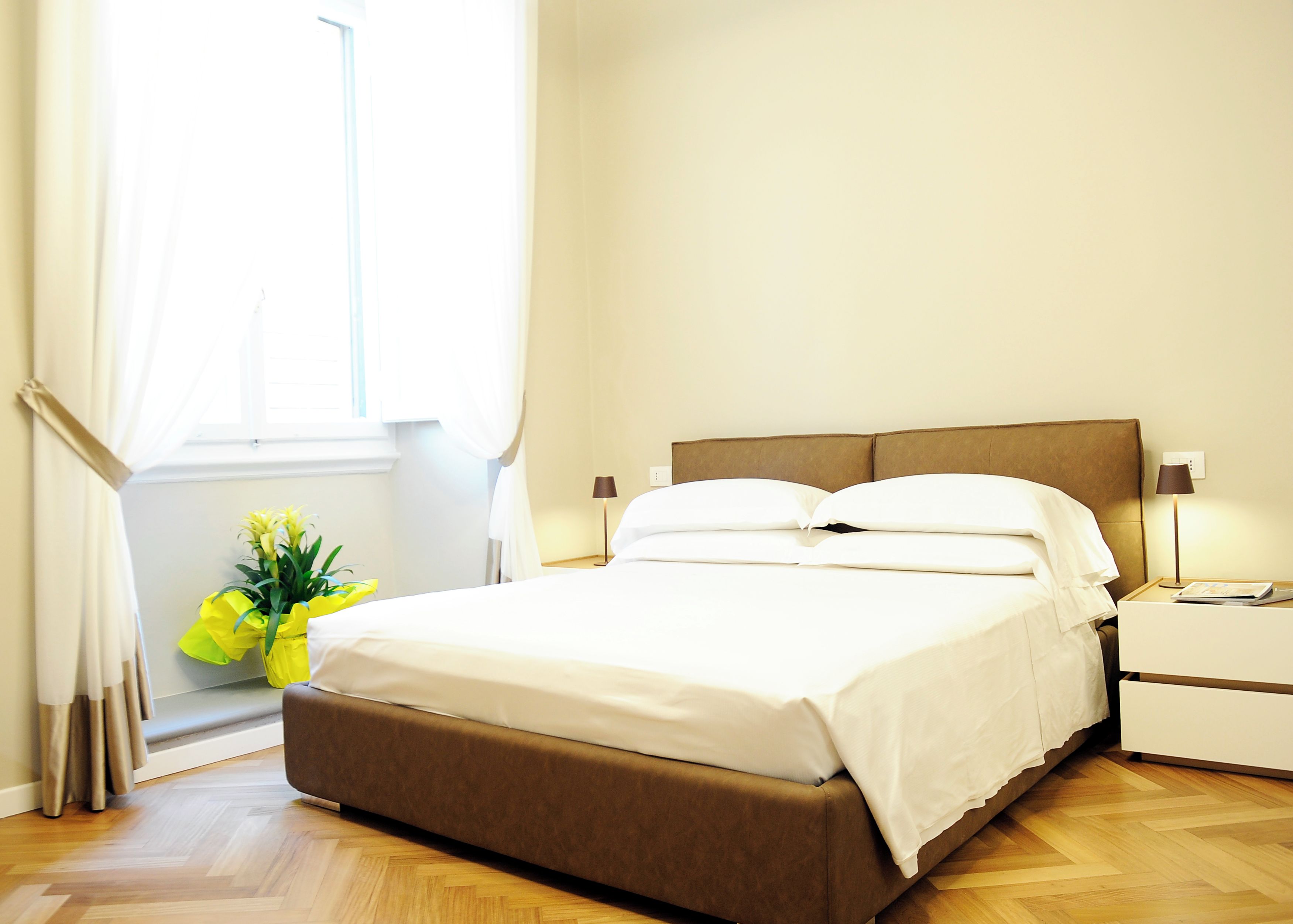A neatly made bed with white linens, a brown headboard, and two bedside lamps.