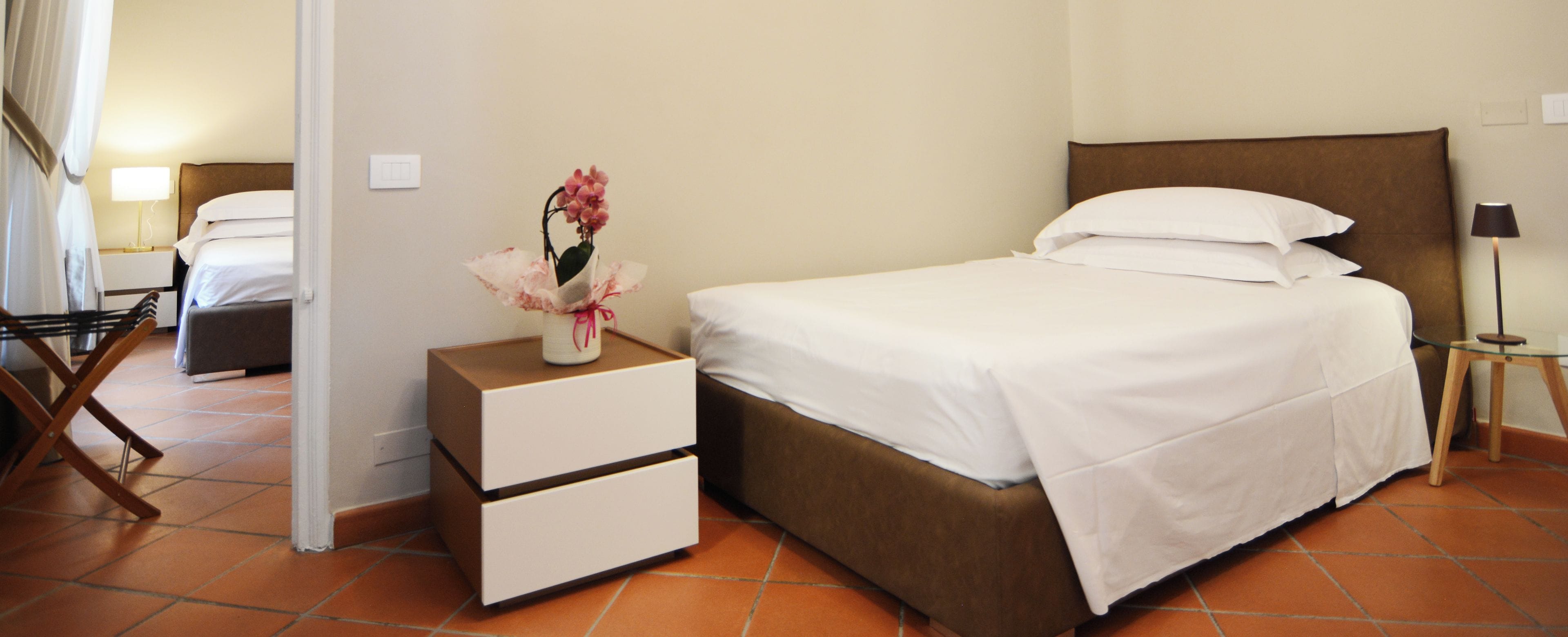 A hotel room with a bed, a nightstand with drawers, a lamp, and a chair.