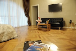 A hotel room with a bed, a sofa, a small table with a magazine, and a TV mounted on the wall.