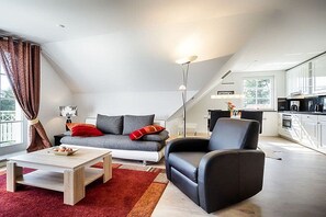 A modern living room with a sofa, armchair, coffee table, and a kitchen in the background. - Holiday apartment with 1 bedroom (Prerow)