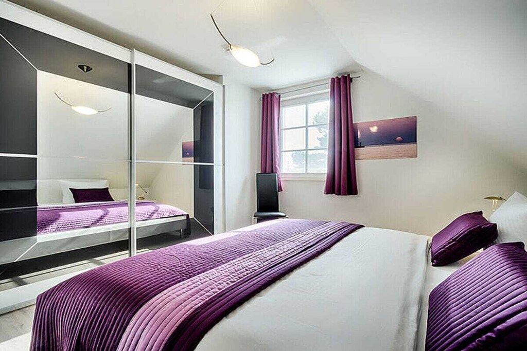 A modern hotel room with a large bed, a glass partition, a desk, and a window with curtains.