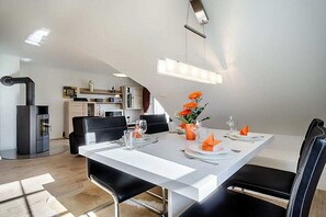 A modern dining area with a white table set for four, black chairs, and a kitchen in the background. - Holiday apartment with 1 bedroom (Prerow)