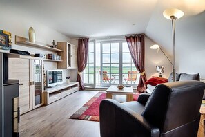 A modern living room with a flat-screen TV, a coffee table, a sofa, and a dining area. - Holiday apartment with 1 bedroom (Prerow)