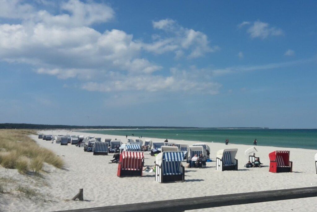 Une plage bordée de rangées de chaises longues et de parasols, une promenade en bois et un ciel dégagé.