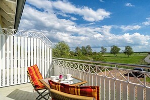 A balcony with a table and chairs, a white railing, and a view of a green landscape. - Holiday apartment with 1 bedroom (Prerow)