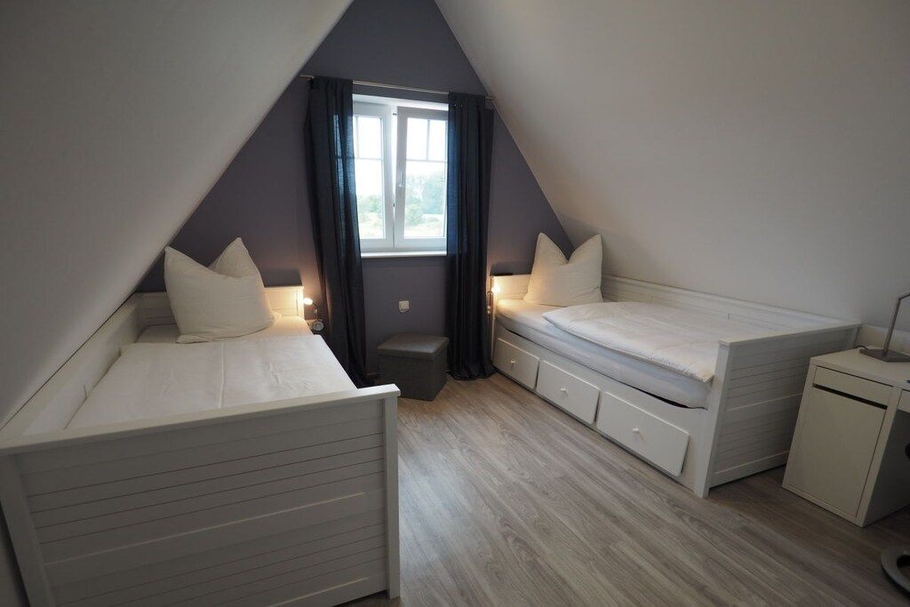 A small, triangular attic bedroom with two beds, a window, and a desk.