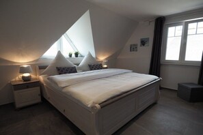 A bedroom with a bed, nightstands, a window, and a small stool. - Dream breeze "Dreaming under thatch" (Ostseebad Rerik)