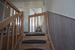 A wooden staircase with a handrail, a landing with a black cushioned seat, and a view into a room with a white door. - Dream breeze "Dreaming under thatch" (Ostseebad Rerik)