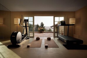 A home gym with exercise equipment, yoga mats, and a view of the outdoors. - Hotel Tschögglbergerhof (San Genesio Atesino)
